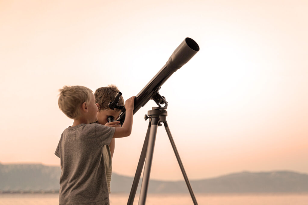 Two children looking up at the sky through a telescope.