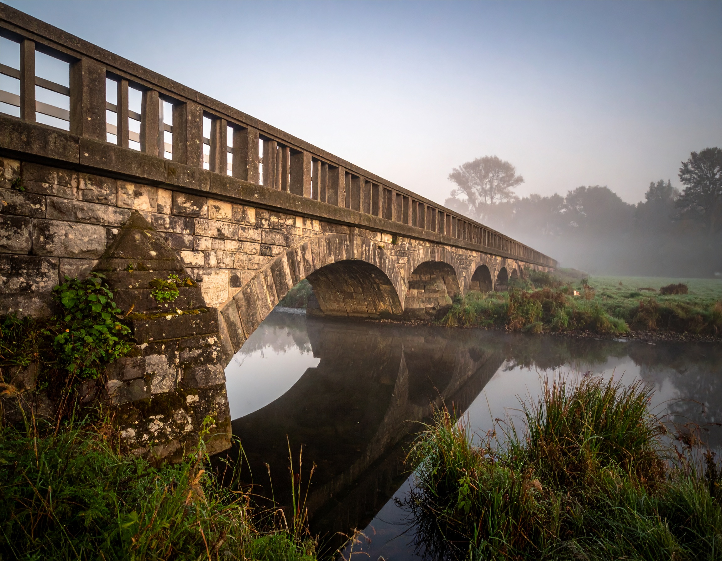 A solid stone bridge spanning a narrow gap photographed in soft morning light with the far bank clearly visible and reachable. Represents the achievable path from NDIS registration to genuine ongoing compliance — with the right IT review and controls in place, closing the gap between registration status and demonstrable compliance is structured, clear, and within reach for providers.