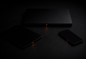 Three different dark professional devices — a closed laptop, a tablet face down, and a smartphone face down — arranged in a precise triangular formation on a near-black surface, each with a single warm amber-orange active indicator LED