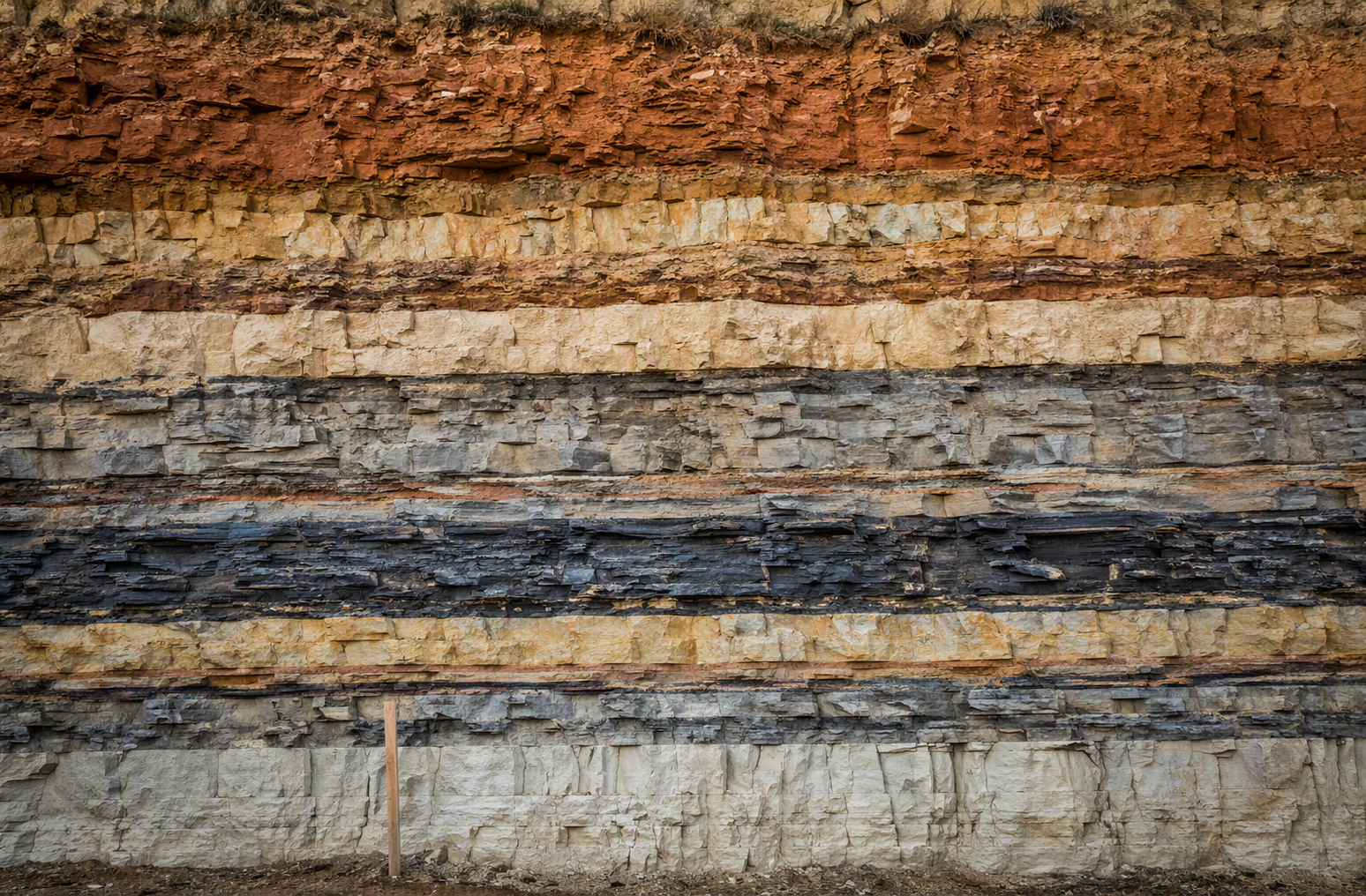 A cross section of exposed rock face showing distinct horizontal geological strata in varying tones of ochre, sandstone, slate, and chalk, representing years of accumulated IT decisions layered invisibly beneath the surface of a portfolio company.